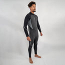 Man wearing Men’s Xenos 7mm black neoprene wetsuit with cutaway ankles and wrist seals, standing barefoot against a gray background